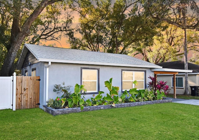 view of front facade featuring a shingled roof, fence, a front lawn, and stucco siding