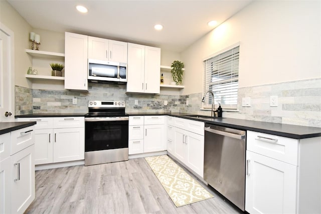 kitchen with white cabinets, dark countertops, stainless steel appliances, open shelves, and a sink