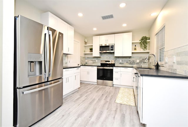 kitchen with appliances with stainless steel finishes, dark countertops, a sink, and open shelves