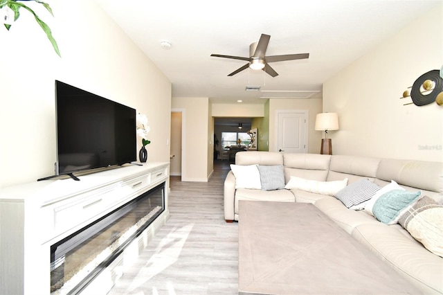 living area with light wood-style floors, a fireplace with flush hearth, visible vents, and ceiling fan