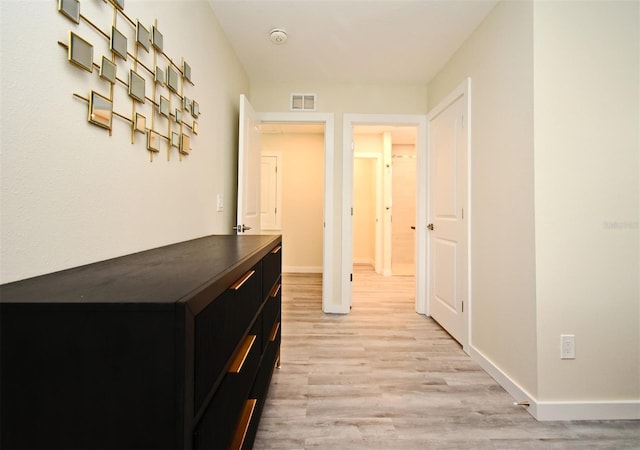 corridor featuring light wood-type flooring, visible vents, and baseboards