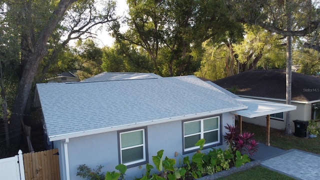 exterior space featuring roof with shingles, fence, and stucco siding