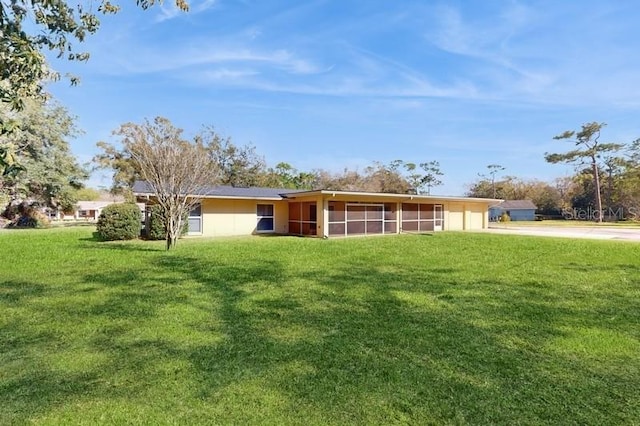 back of house featuring driveway, a sunroom, an attached garage, and a lawn