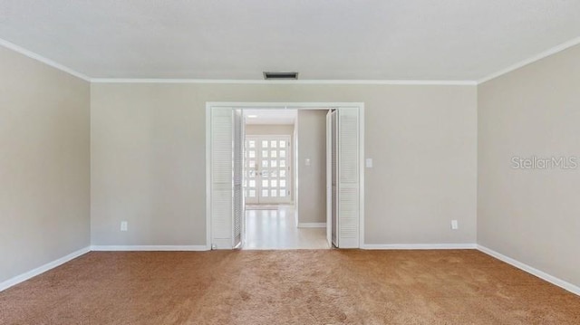 spare room featuring carpet floors, ornamental molding, visible vents, and baseboards