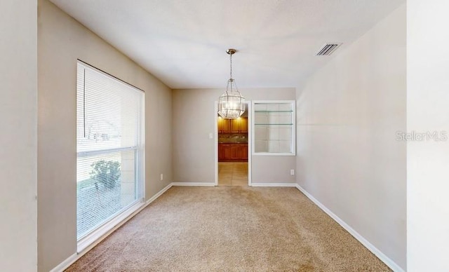 empty room featuring light carpet, a chandelier, visible vents, and baseboards