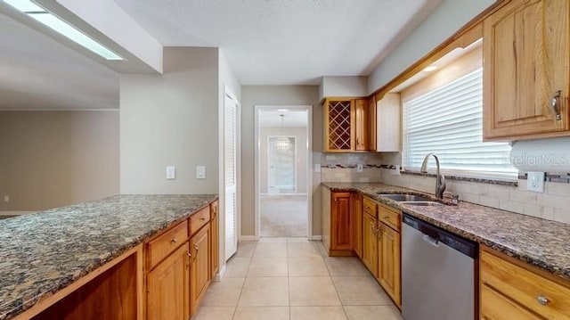 kitchen with light tile patterned floors, dark stone counters, a sink, backsplash, and dishwasher