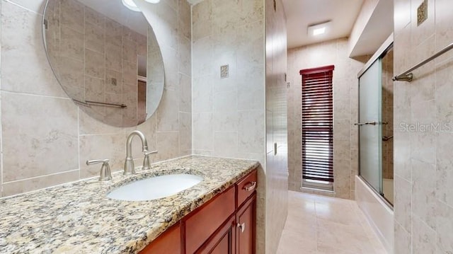 full bathroom with tile patterned flooring, enclosed tub / shower combo, tile walls, and vanity