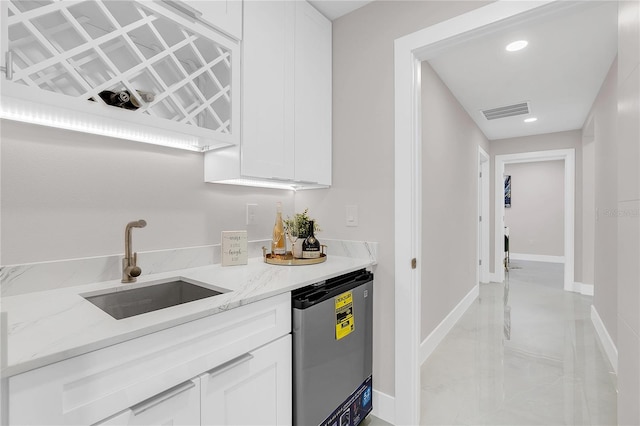 kitchen featuring white cabinetry, baseboards, a sink, dishwashing machine, and light stone countertops