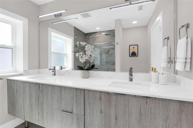 bathroom with a marble finish shower, double vanity, visible vents, and a sink