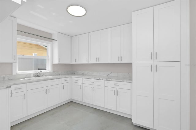 kitchen featuring white cabinets, a sink, light stone counters, and finished concrete floors