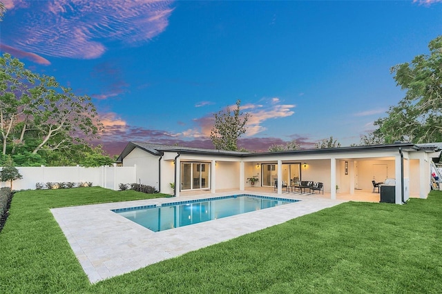 back of house at dusk featuring a patio, stucco siding, fence, and a yard