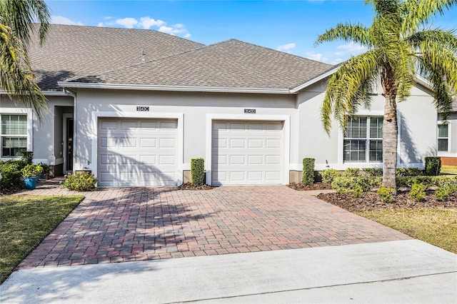 view of front of property with roof with shingles, decorative driveway, an attached garage, and stucco siding