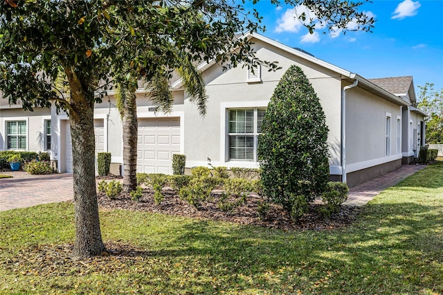 view of side of home featuring a garage, decorative driveway, a lawn, and stucco siding