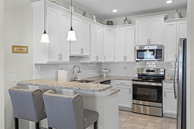 kitchen with a peninsula, a sink, white cabinetry, a kitchen breakfast bar, and appliances with stainless steel finishes