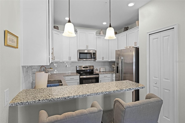 kitchen with light stone counters, backsplash, appliances with stainless steel finishes, a sink, and a peninsula