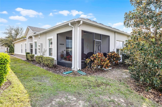 view of side of home with a lawn, a sunroom, and stucco siding