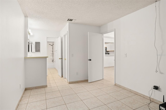 unfurnished room featuring light tile patterned floors, baseboards, visible vents, and a textured ceiling