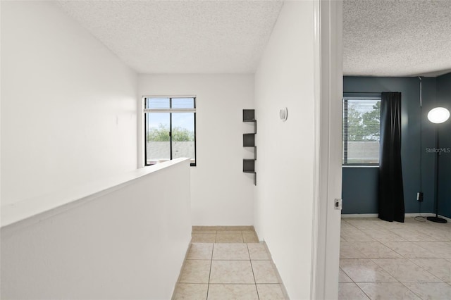 hallway with light tile patterned floors, a textured ceiling, a wealth of natural light, and baseboards