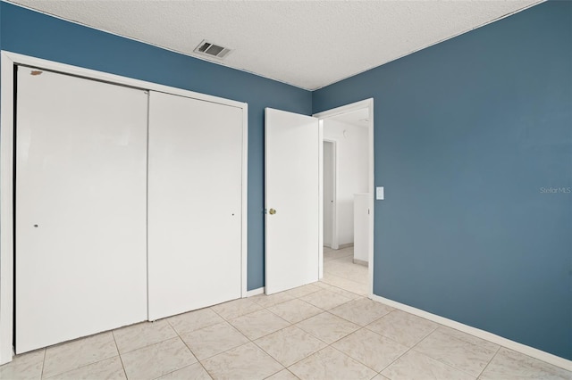 unfurnished bedroom featuring a textured ceiling, light tile patterned flooring, visible vents, baseboards, and a closet