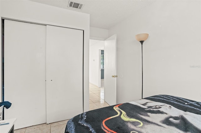 bedroom featuring a closet, visible vents, a textured ceiling, and light tile patterned flooring