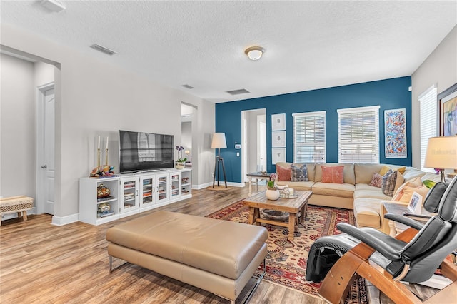 living area with baseboards, a textured ceiling, visible vents, and wood finished floors