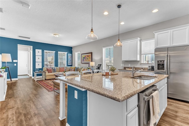 kitchen featuring wood finished floors, a sink, white cabinetry, appliances with stainless steel finishes, and a center island with sink