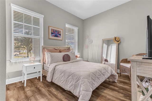 bedroom with multiple windows, wood finished floors, and baseboards