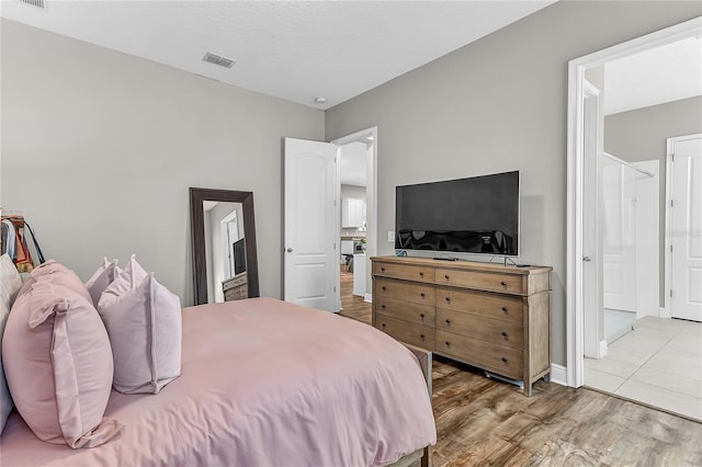 bedroom featuring ensuite bath, wood finished floors, and visible vents