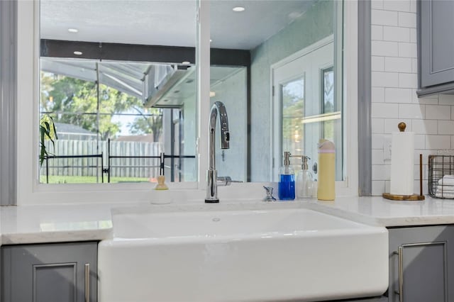 interior space with a sink, light stone counters, tasteful backsplash, and gray cabinets