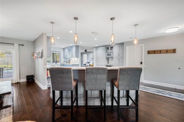 kitchen with dark wood finished floors, light countertops, a breakfast bar area, and baseboards