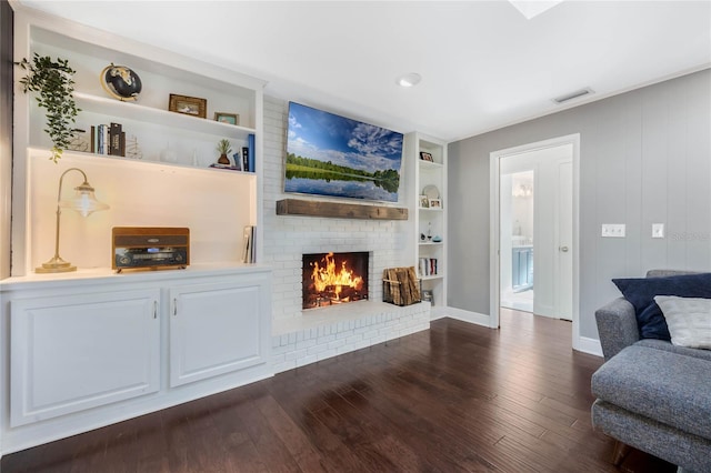 living area with dark wood-style floors, visible vents, a fireplace, and built in shelves