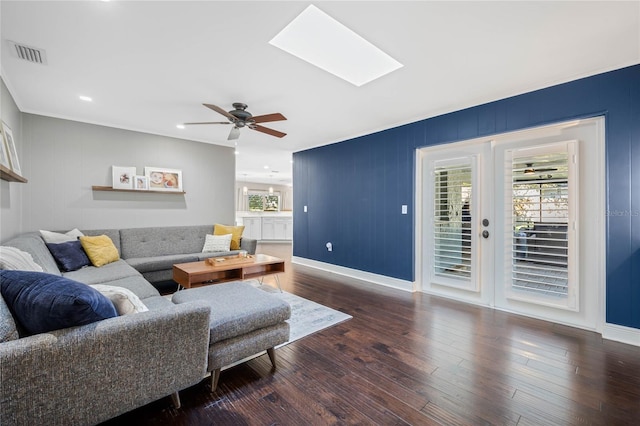 living room with a ceiling fan, wood finished floors, visible vents, baseboards, and a skylight