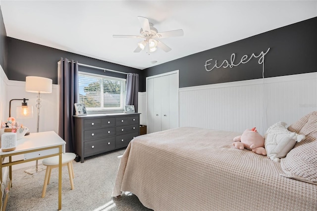 bedroom featuring a closet, wainscoting, carpet, and ceiling fan