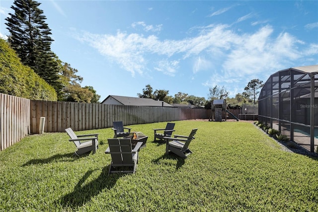 view of yard with glass enclosure, an outdoor fire pit, a playground, and a fenced backyard