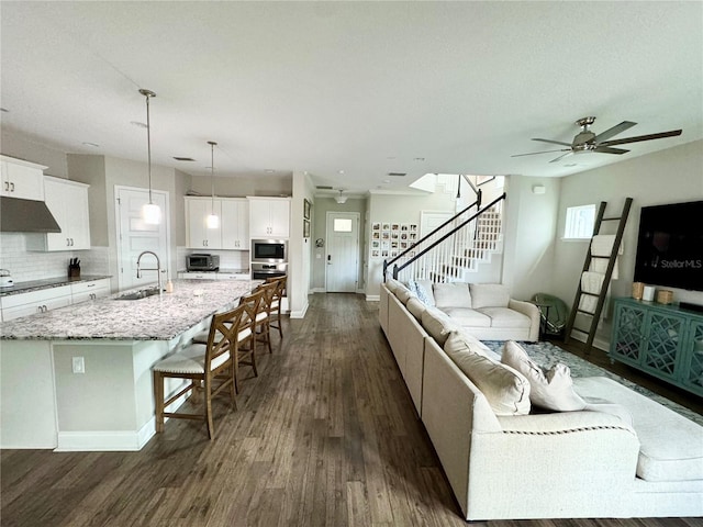 living area with a toaster, a ceiling fan, baseboards, stairs, and dark wood finished floors