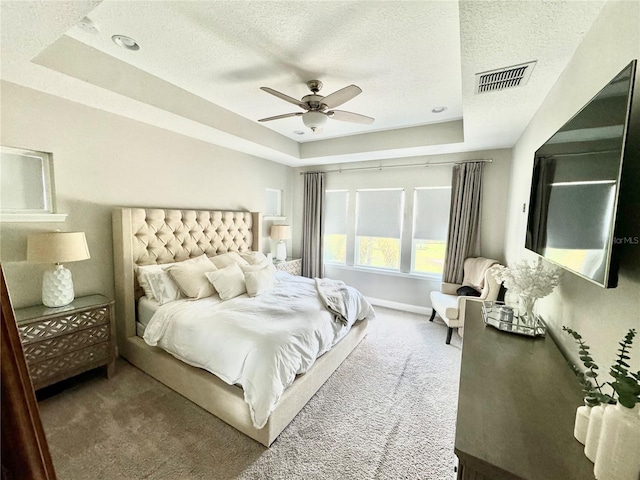 carpeted bedroom featuring a textured ceiling, a raised ceiling, visible vents, and baseboards