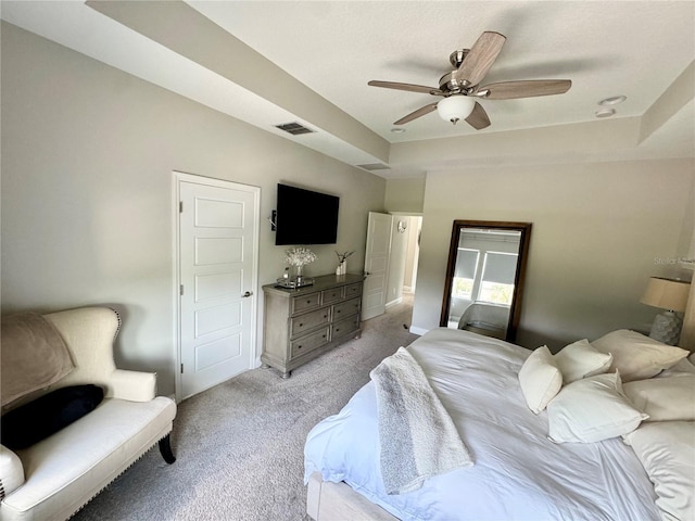 bedroom featuring light colored carpet, a tray ceiling, visible vents, and ceiling fan