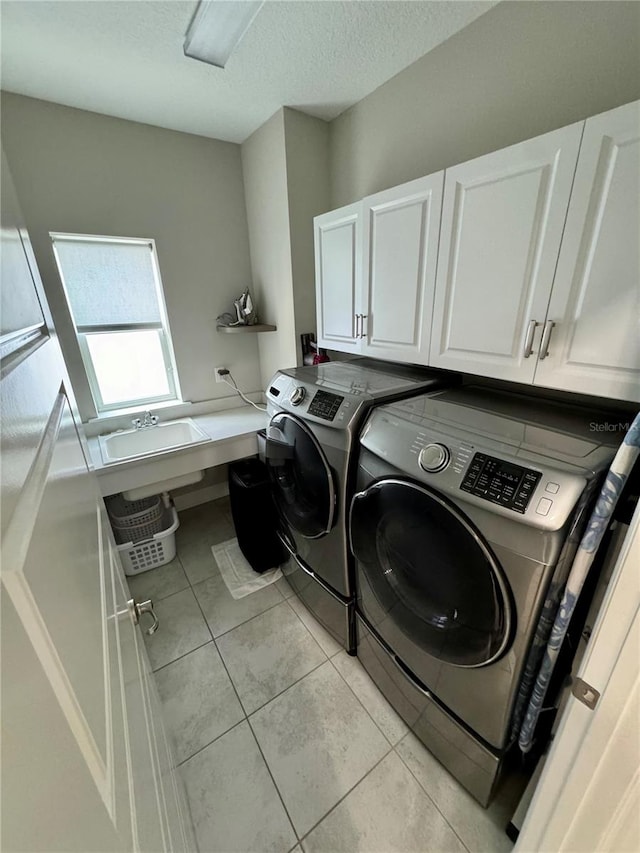 laundry room featuring cabinet space, light tile patterned floors, washing machine and clothes dryer, a textured ceiling, and a sink