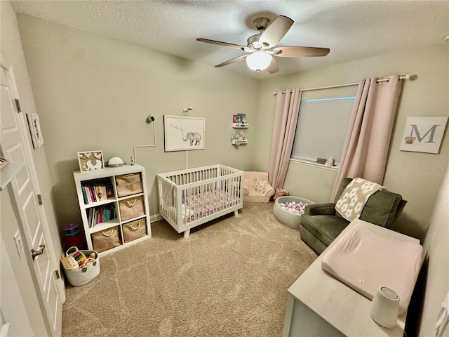 carpeted bedroom with a crib, ceiling fan, and a textured ceiling