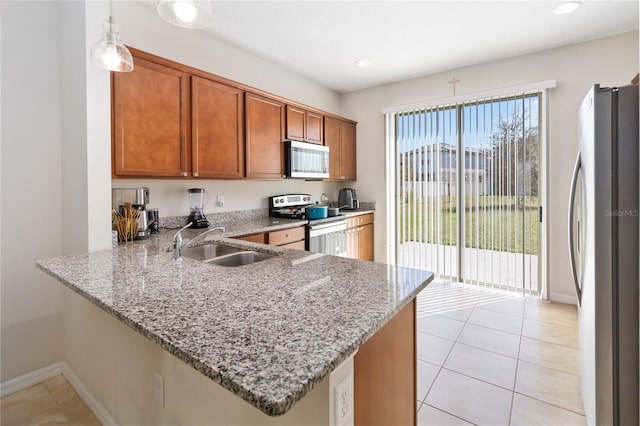 kitchen featuring light tile patterned floors, brown cabinets, a peninsula, stainless steel appliances, and a sink