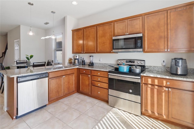 kitchen featuring stainless steel appliances, a peninsula, light stone countertops, and brown cabinets