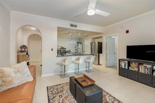 living area featuring light tile patterned floors, visible vents, baseboards, a ceiling fan, and crown molding