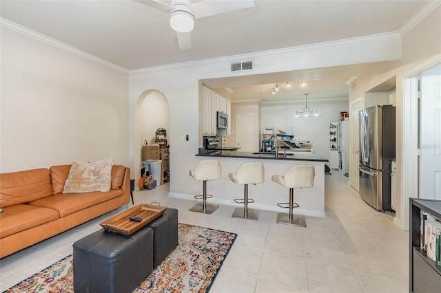 living area featuring arched walkways, light tile patterned floors, ceiling fan with notable chandelier, visible vents, and crown molding