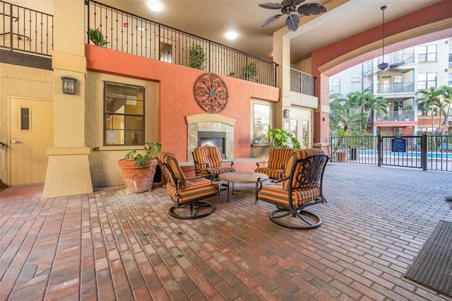 view of patio / terrace featuring a ceiling fan, a tile fireplace, fence, and a community pool