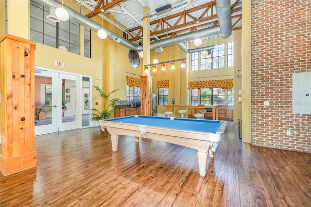 recreation room with a towering ceiling, brick wall, billiards, and wood finished floors