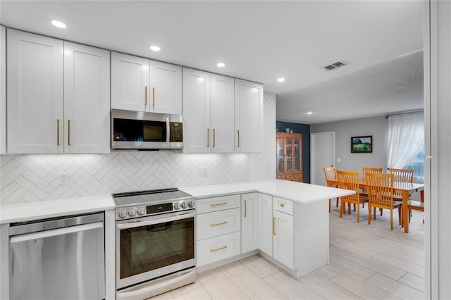 kitchen with stainless steel appliances, a peninsula, light countertops, and visible vents