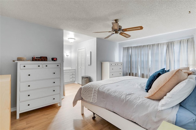 bedroom featuring light wood finished floors, ceiling fan, ensuite bathroom, a textured ceiling, and a closet