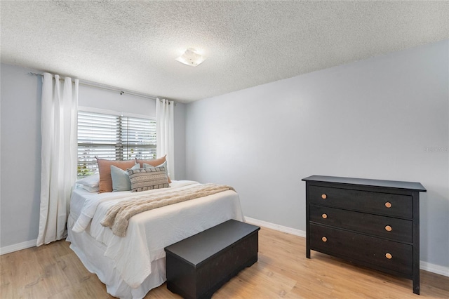 bedroom featuring light wood-style flooring, baseboards, and a textured ceiling