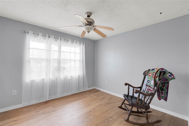 living area with a textured ceiling, baseboards, and wood finished floors