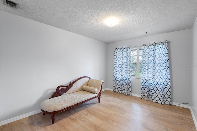 living area with a textured ceiling, wood finished floors, visible vents, and baseboards